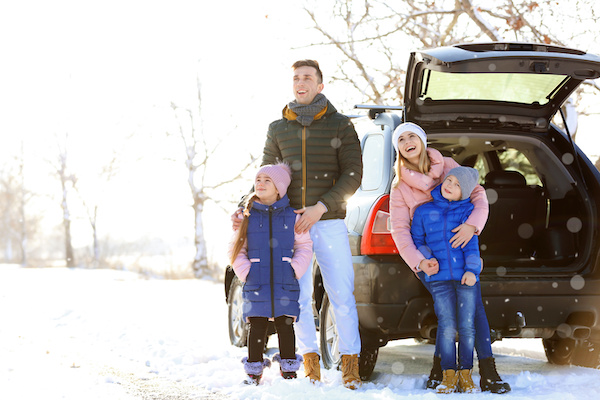 A happy family wearing winter clothes outside their SUV in the snow